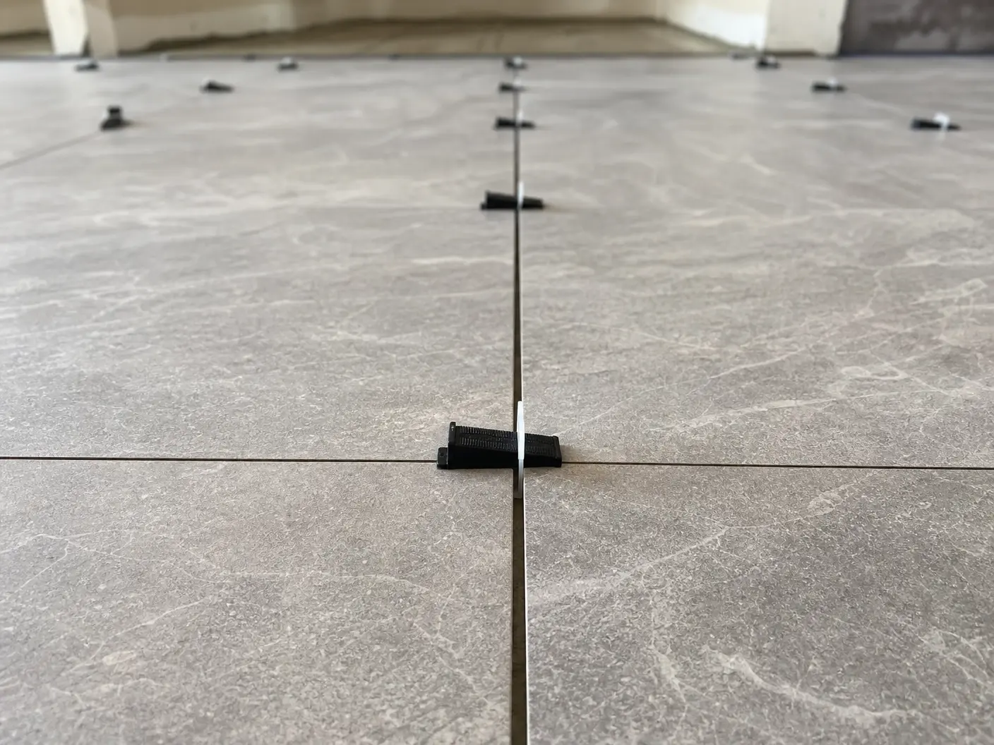 Large-format porcelain floor mid-installation, levelling clips still in place, joints running dead straight