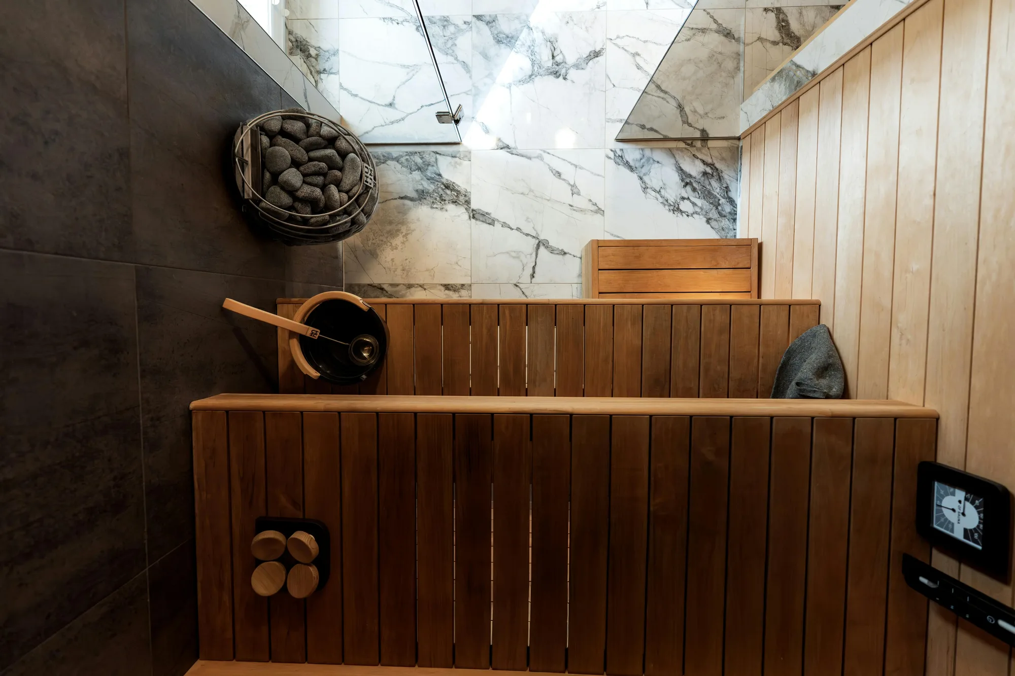 Home sauna finished in cedar with a book-matched marble wall and dark large-format tile