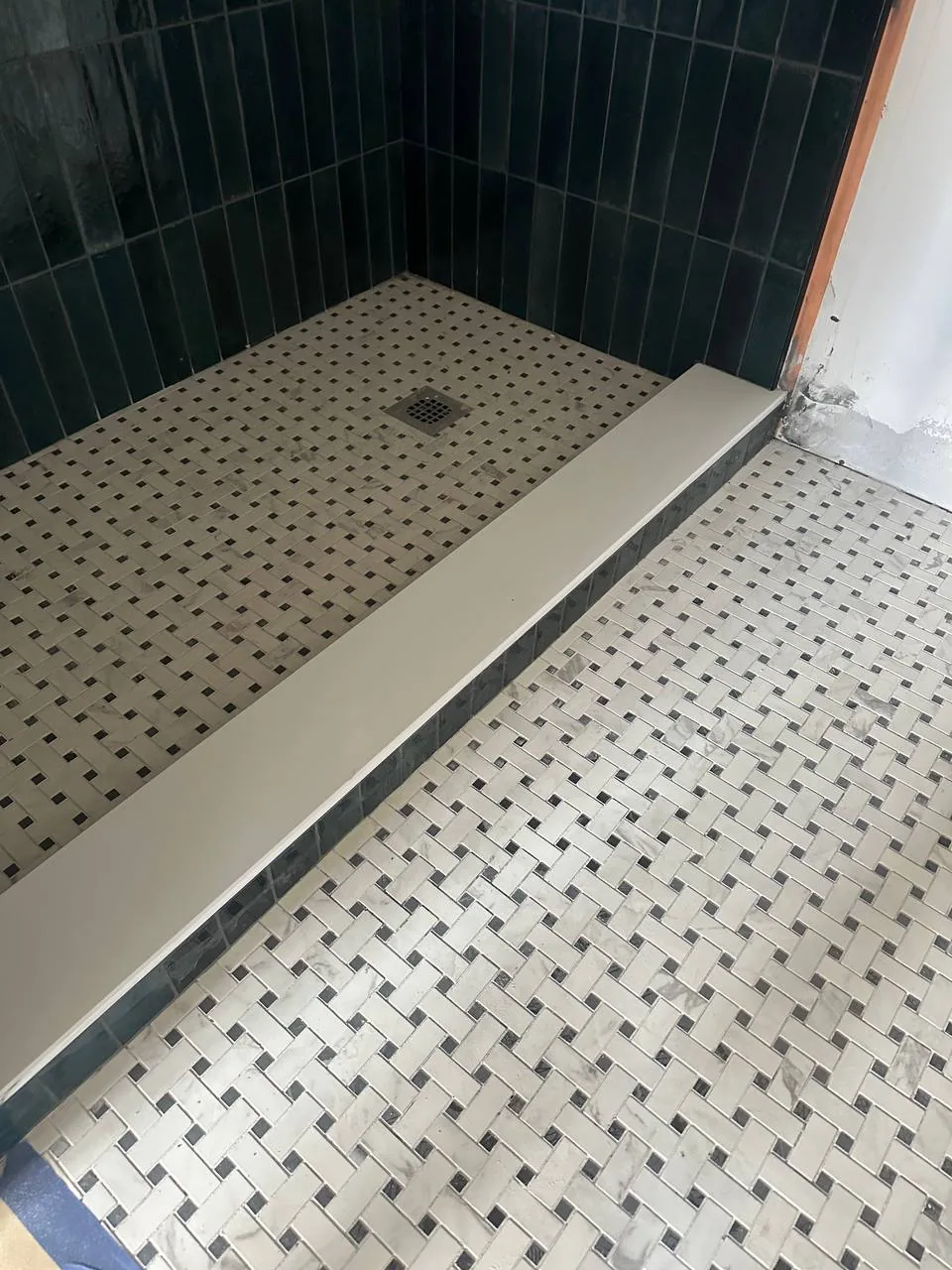 Basketweave marble mosaic shower floor meeting a dark green tiled wall at a low kerb