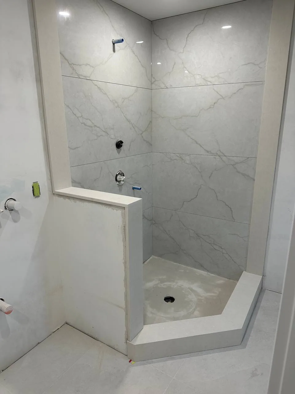 Finished walk-in shower in marble-look porcelain with a half wall and a curbless entry