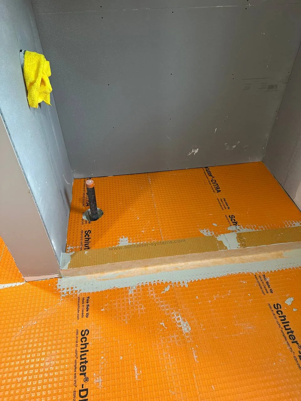 Heating membrane bedded across a bathroom floor and up to the base of the walls