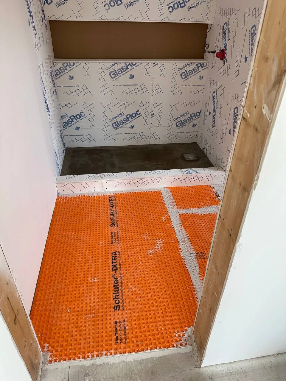 Orange uncoupling membrane bedded across the shower floor and out onto the bathroom floor