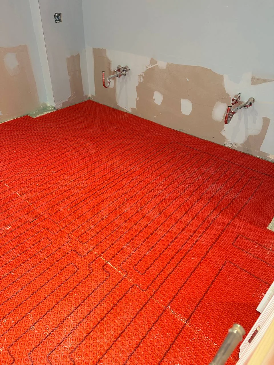 Electric heating cable run into an orange membrane across an entire bathroom floor