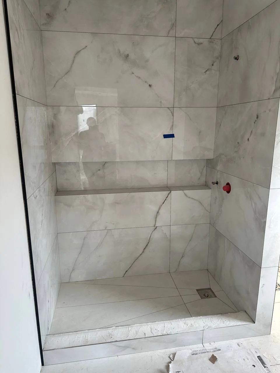 Finished shower with a full-width porcelain bench and a recessed shampoo shelf, veins running through the joints
