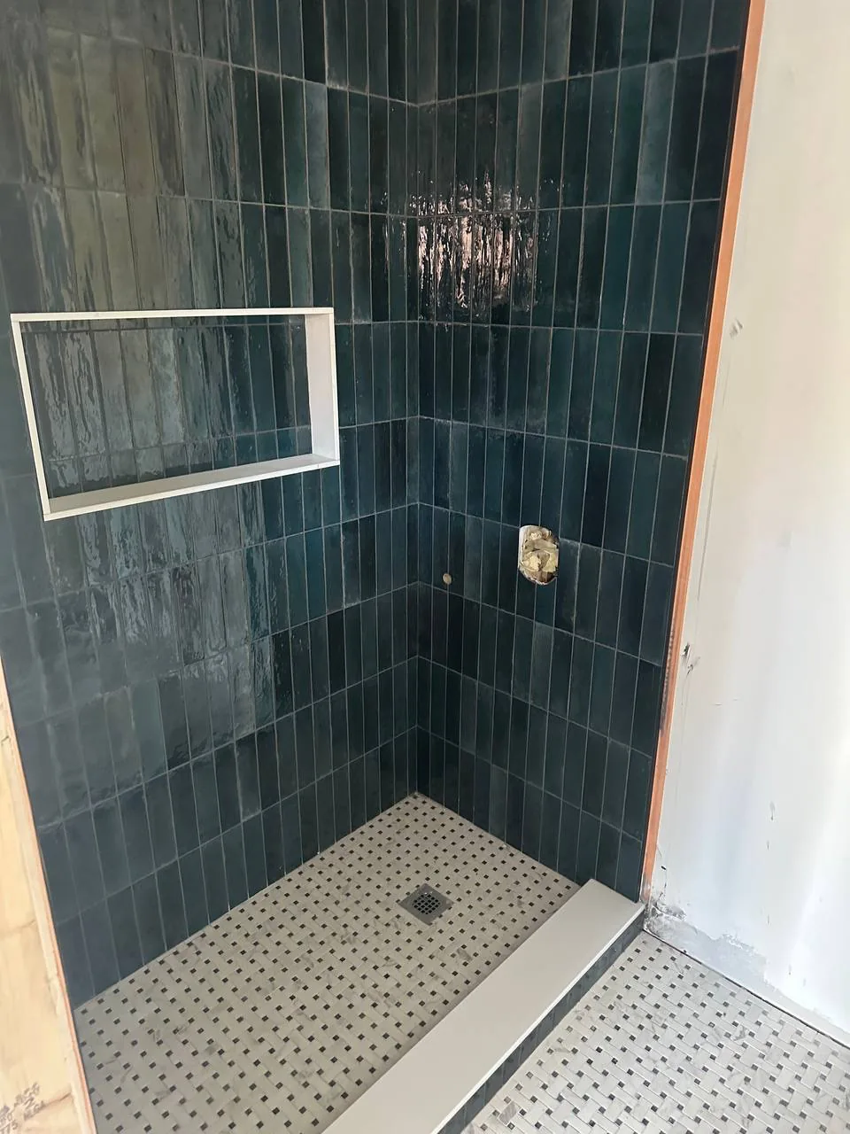 Dark green handmade-look tile stacked vertically up a shower wall with a recessed niche