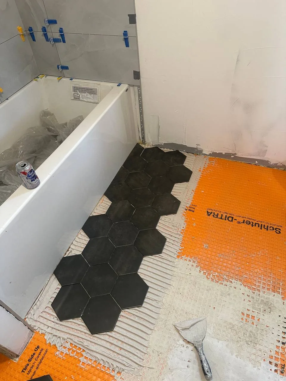 Black hexagon tile being laid out from an orange uncoupling membrane along a bath