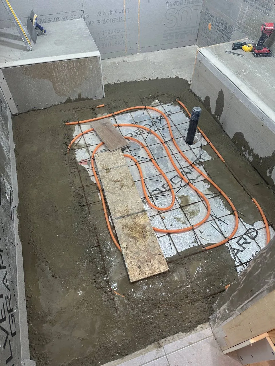 Orange PEX heating loops tied out to reinforcing mesh across an insulated basement floor before the pour