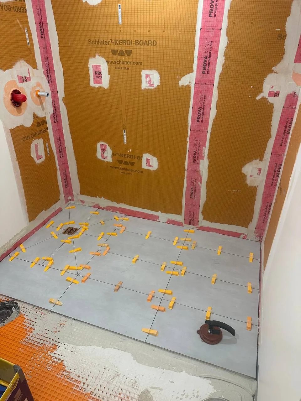 Waterproof board shower walls above a tiled floor held out with orange levelling clips