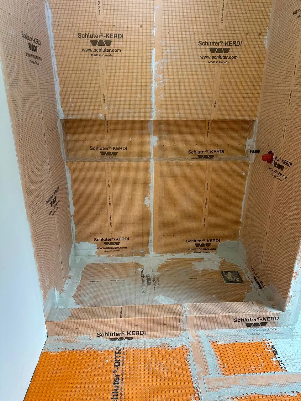 Shower walls and niche fully covered in bonded orange waterproofing membrane, seams banded