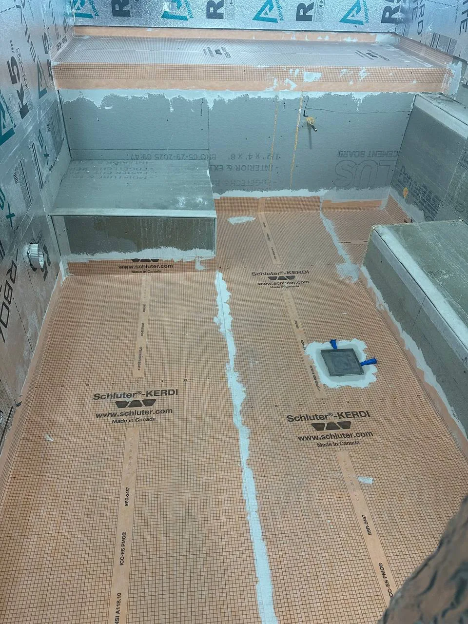 Poured concrete benches and floor covered in bonded waterproofing membrane around a linear drain