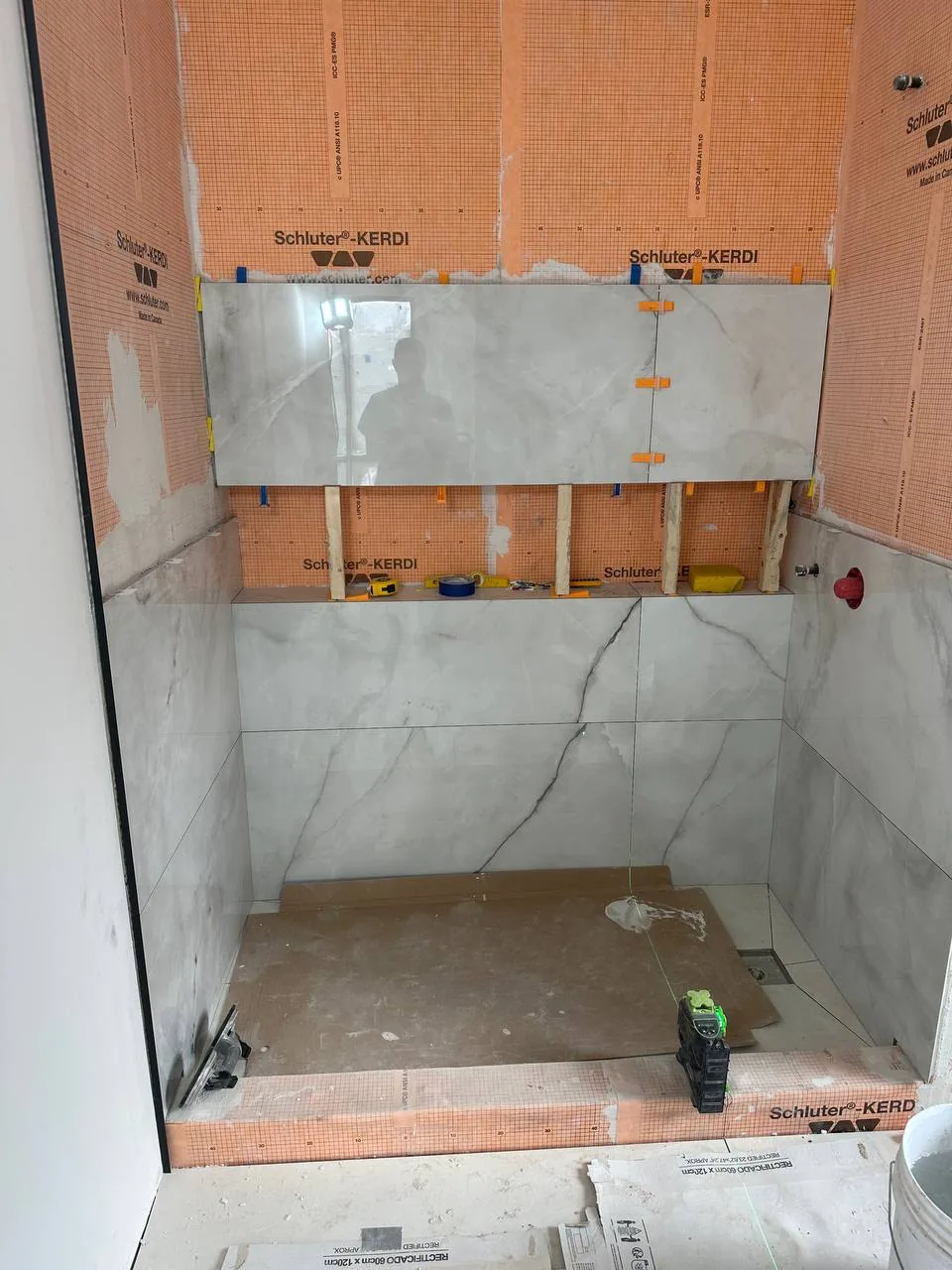 Large-format marble-look porcelain going up a shower wall with levelling clips holding the plane
