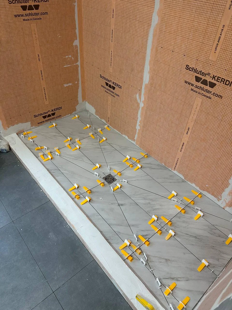 Linear drain set at the wall of a shower with the tile falling towards it in one plane