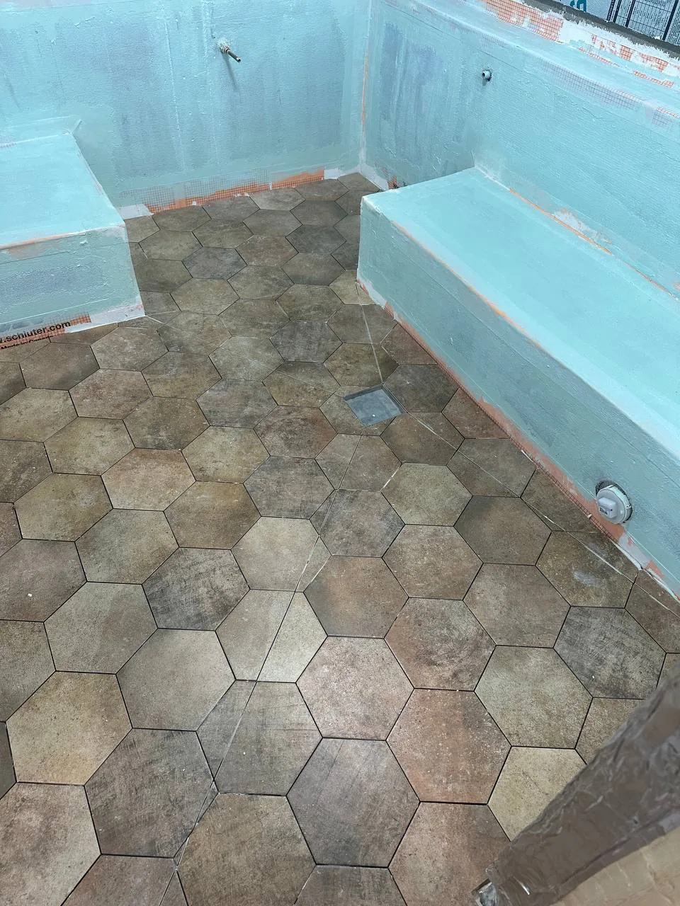 Second liquid waterproofing coat in blue applied over the benches and walls of a wet room