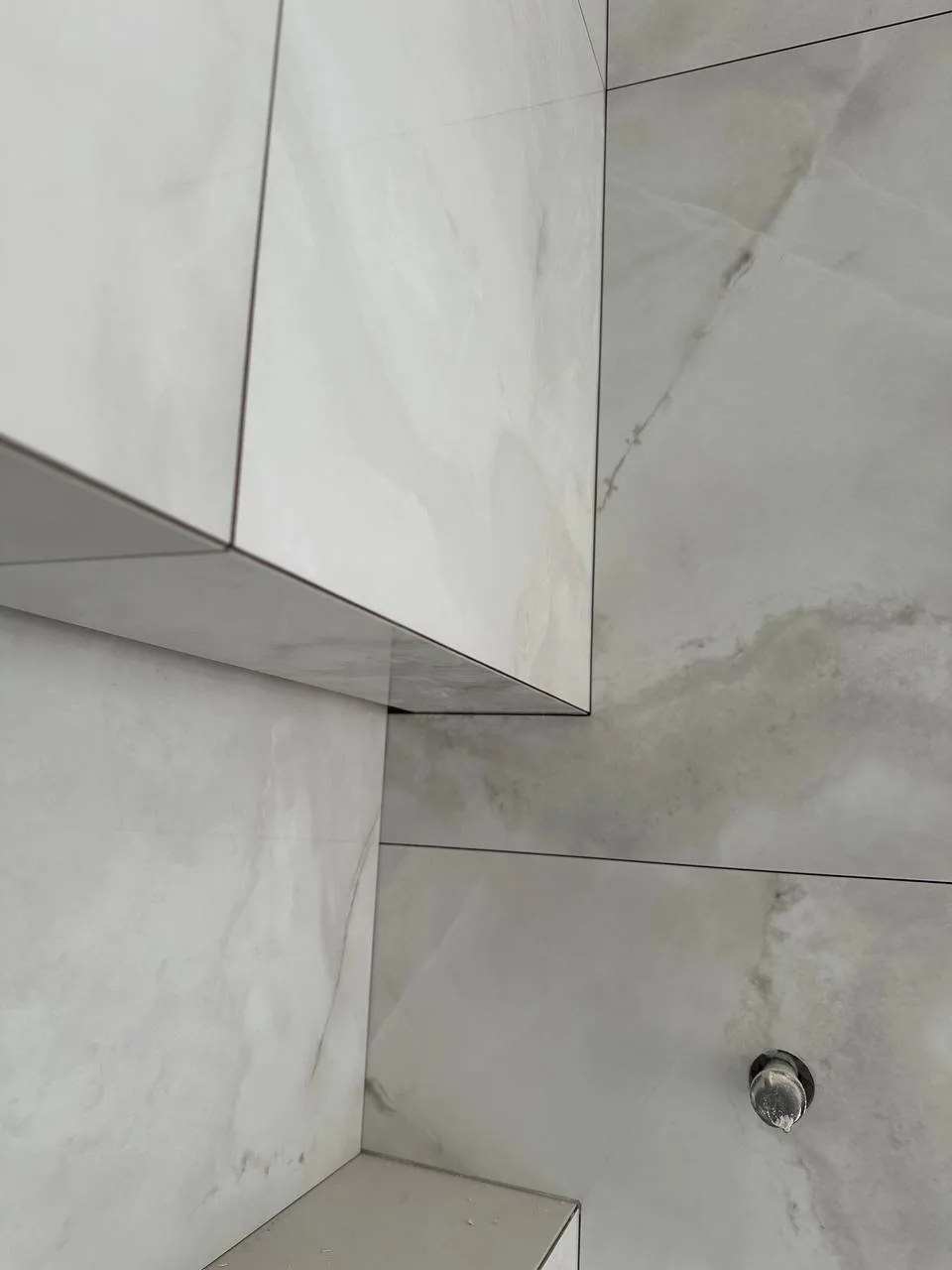 Close view of a shower bench edge where two porcelain slabs meet in a mitred 45-degree joint