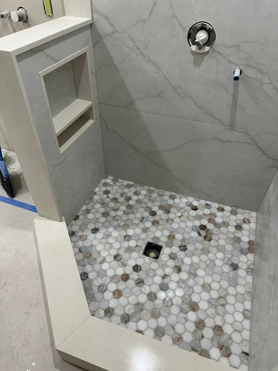 Shower floor in round pebble mosaic against large-format marble-look walls and a built-in niche