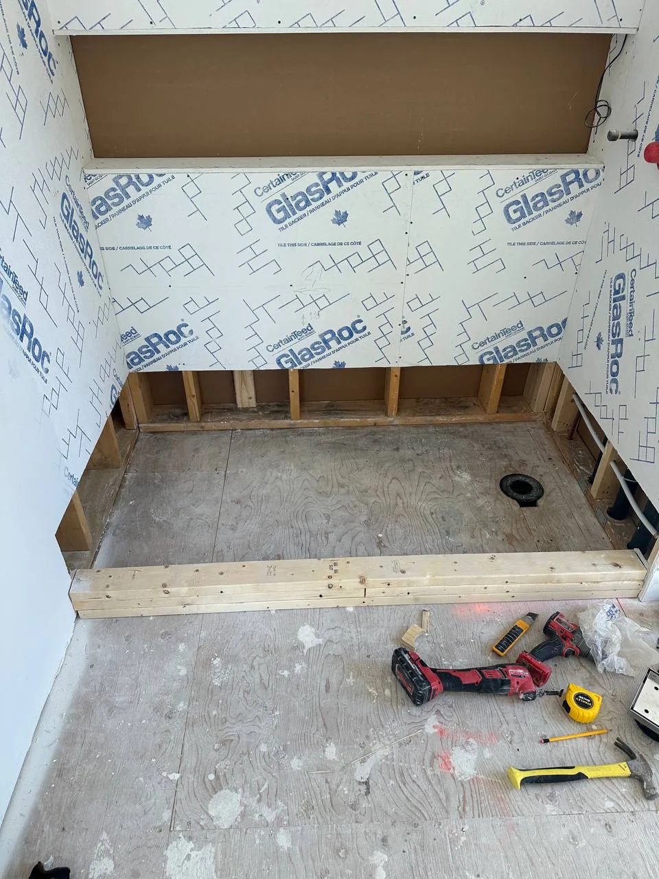 Timber curb and blocking framed at the base of a shower opening, subfloor stripped back to bare board